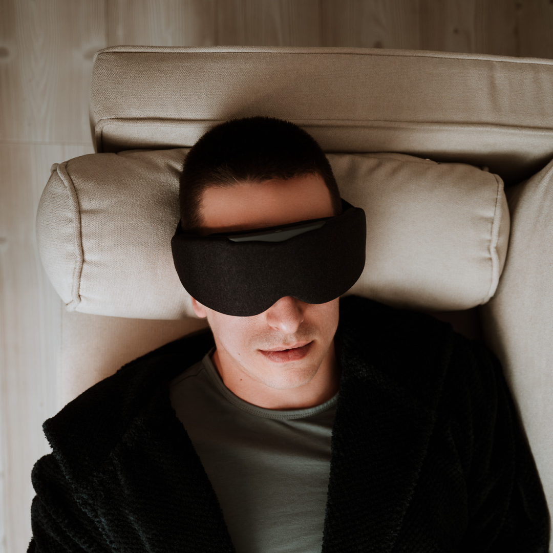 Man lying on a sofa and Relaxing with Aura Smart Sleep Mask in Grey